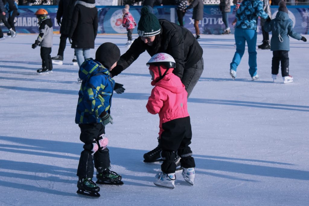 2 children in red jacket and black pants playing ice hockey